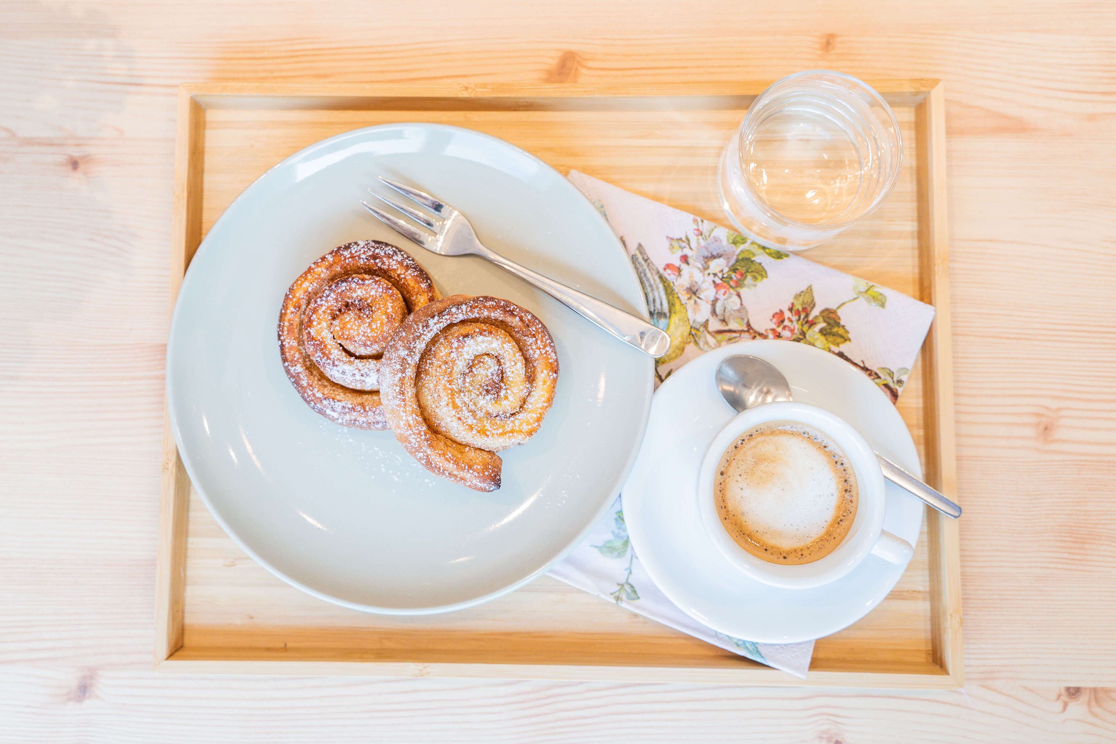 Ett bricka med en tallrik kanelbullar och en kopp kaffe på ett träbord.