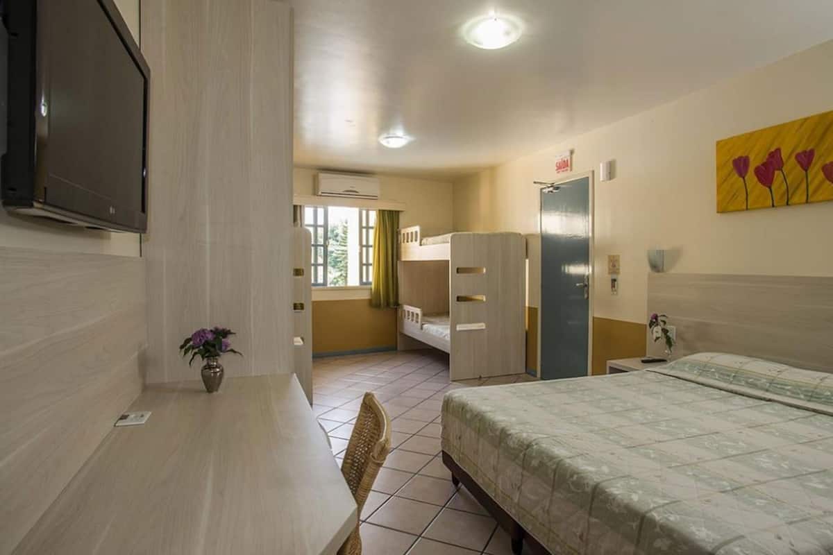Hotellihuone, jossa on sänky, työpöytä, tuoli, televisio, ikkuna ja ovi.