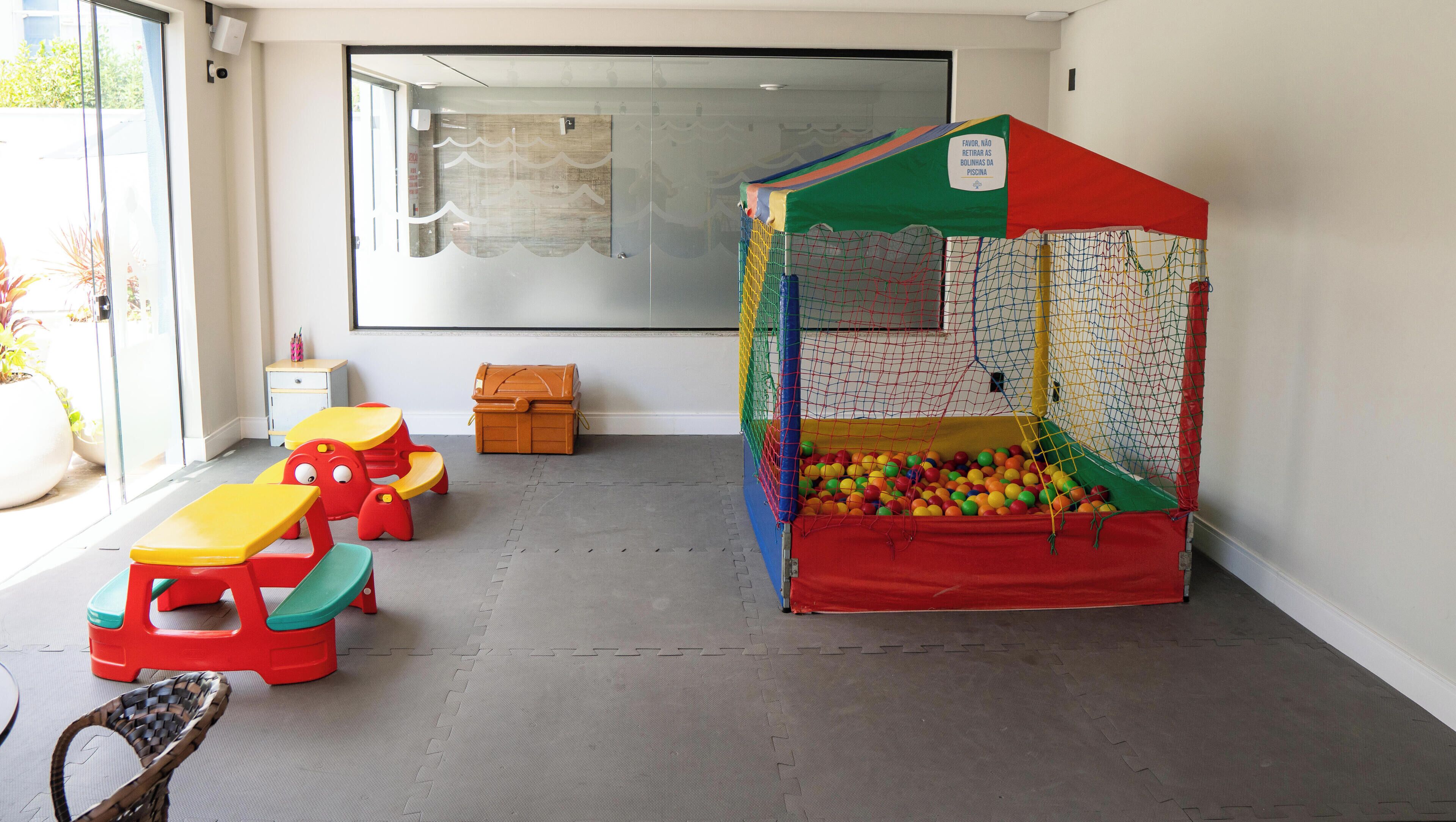 A children's play area with a ball pit and a climbing net, a window with a view, and a table with chairs.