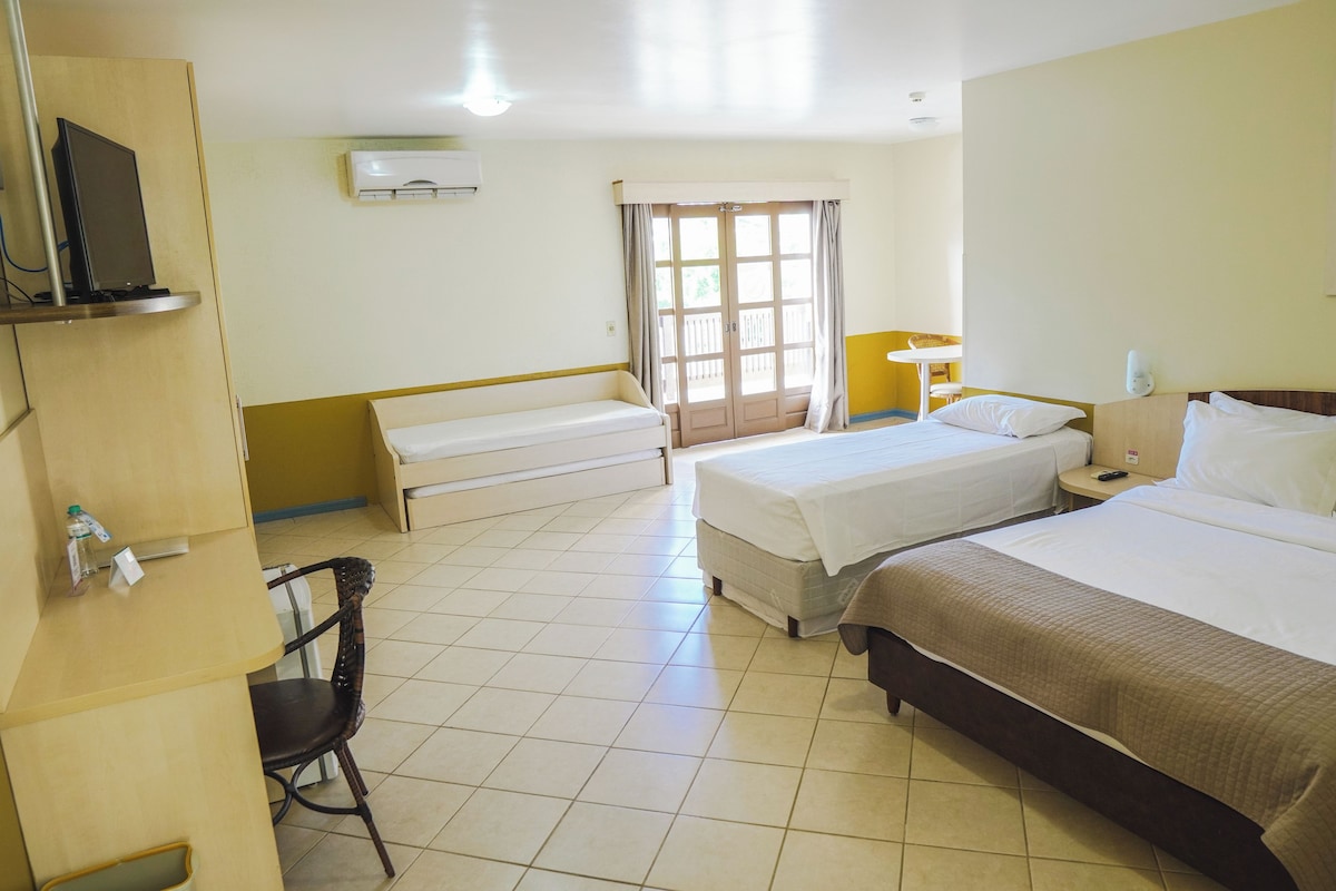 Habitación de hotel con dos camas, un escritorio, una silla, un televisor y una ventana con cortinas.