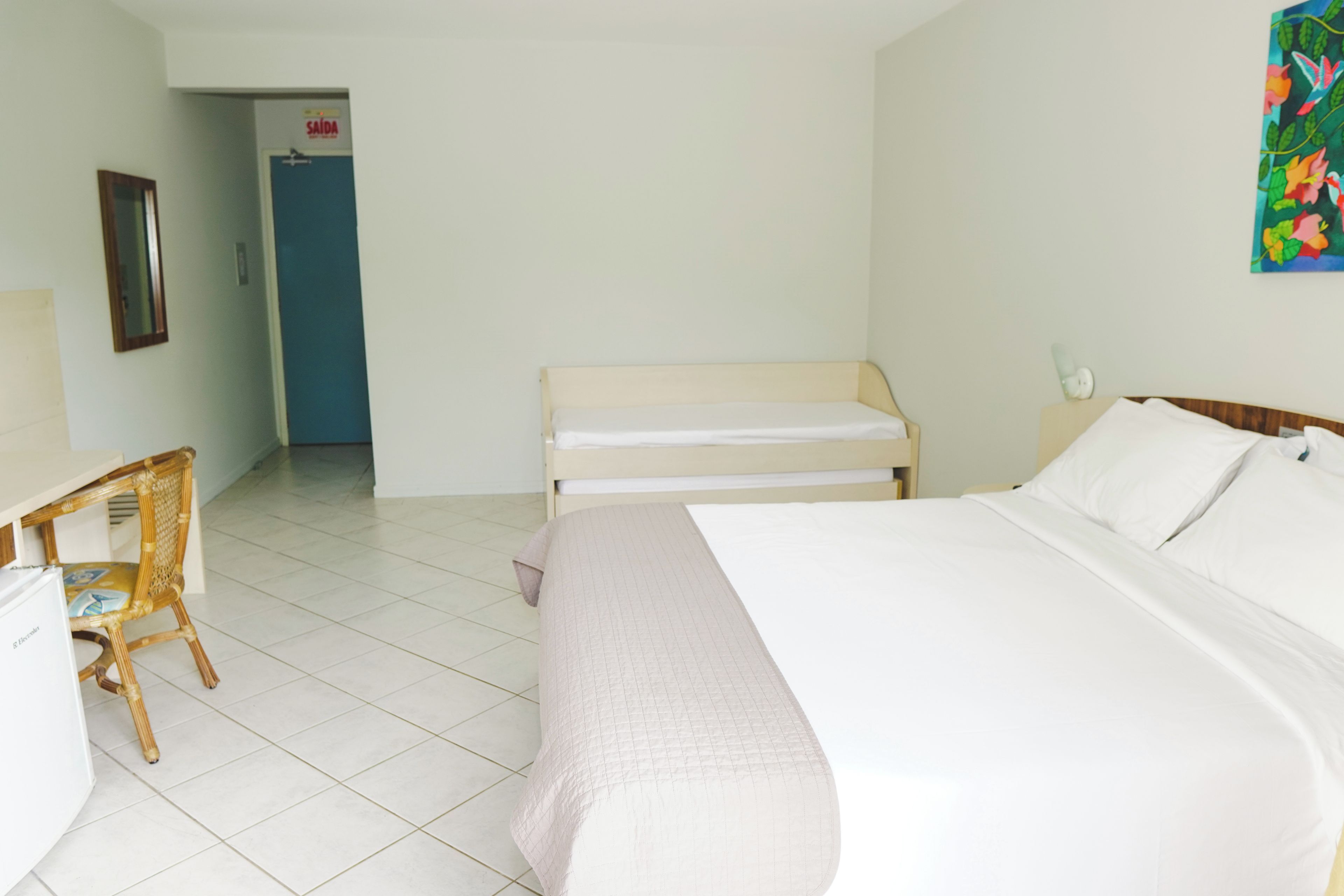 A hotel room with a bed, a chair, a desk, and a door.