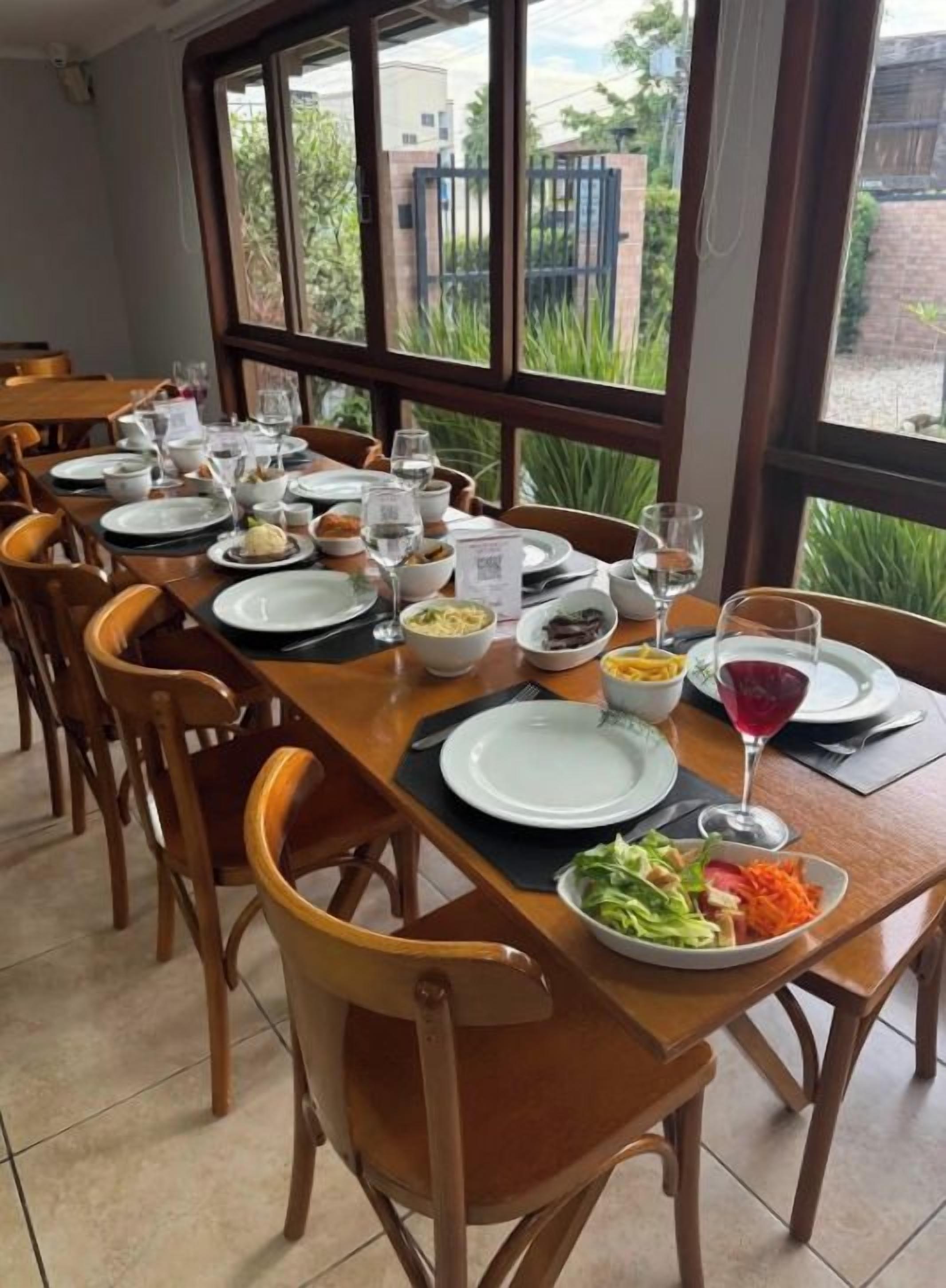 A dining area with multiple tables set for meals, chairs, and a view through large windows.
