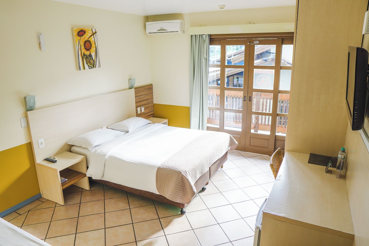 Habitación de hotel con una cama, una mesita de noche, un televisor, una ventana con vistas y un aire acondicionado de pared.