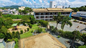 A courtyard with a volleyball court, surrounded by greenery and a building with a tiled roof. - Vila Olaria Hotel (Penha)