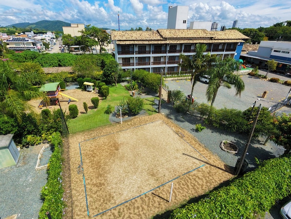 A courtyard with a volleyball court, surrounded by greenery and a building with a tiled roof. - Vila Olaria Hotel (Penha)