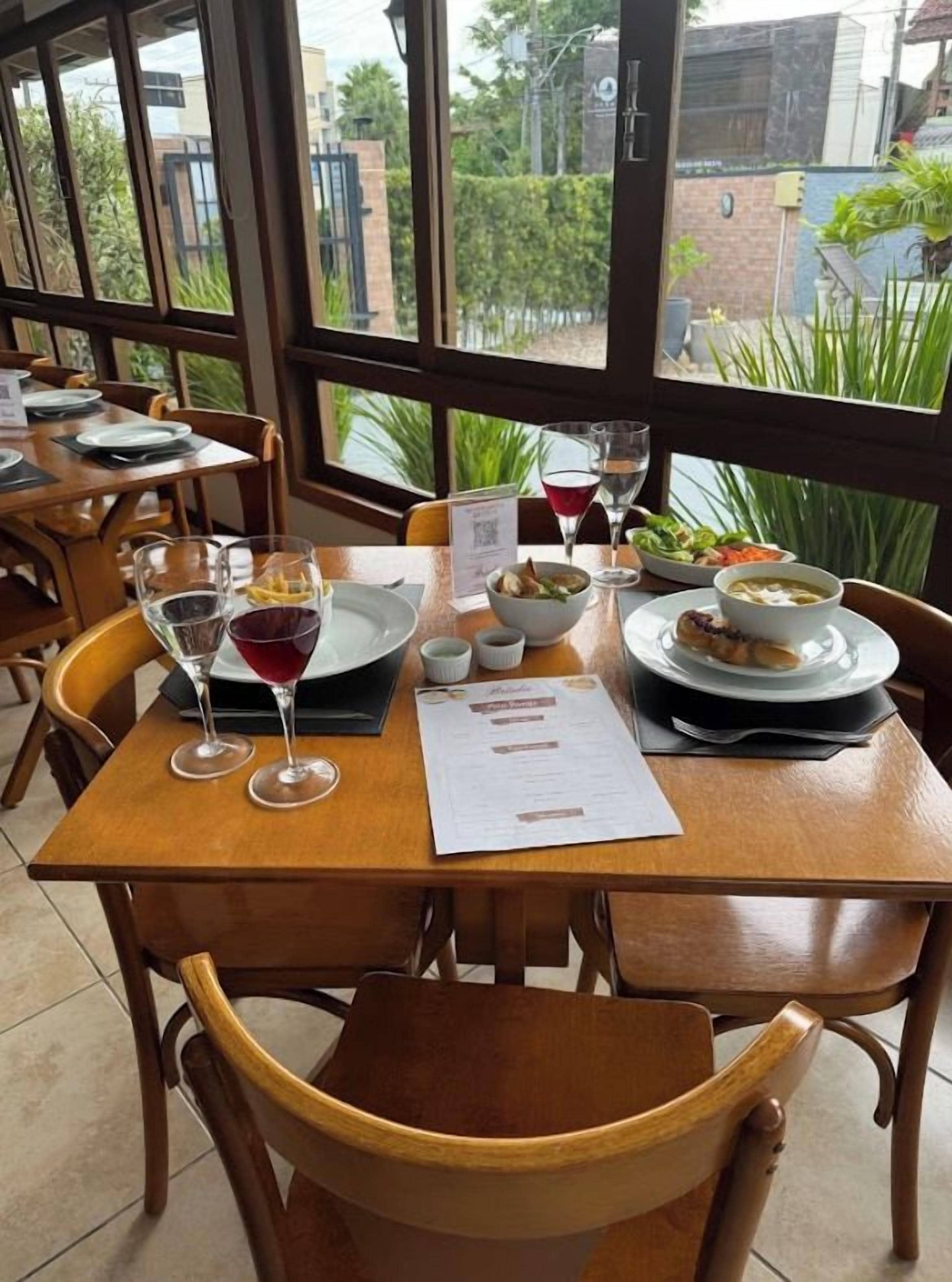 A restaurant table set with a menu, wine glasses, and plates of food.