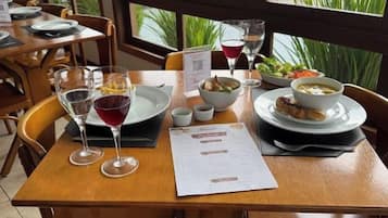 Uma mesa de restaurante posta, com cardápio, copos de vinho e pratos de comida.