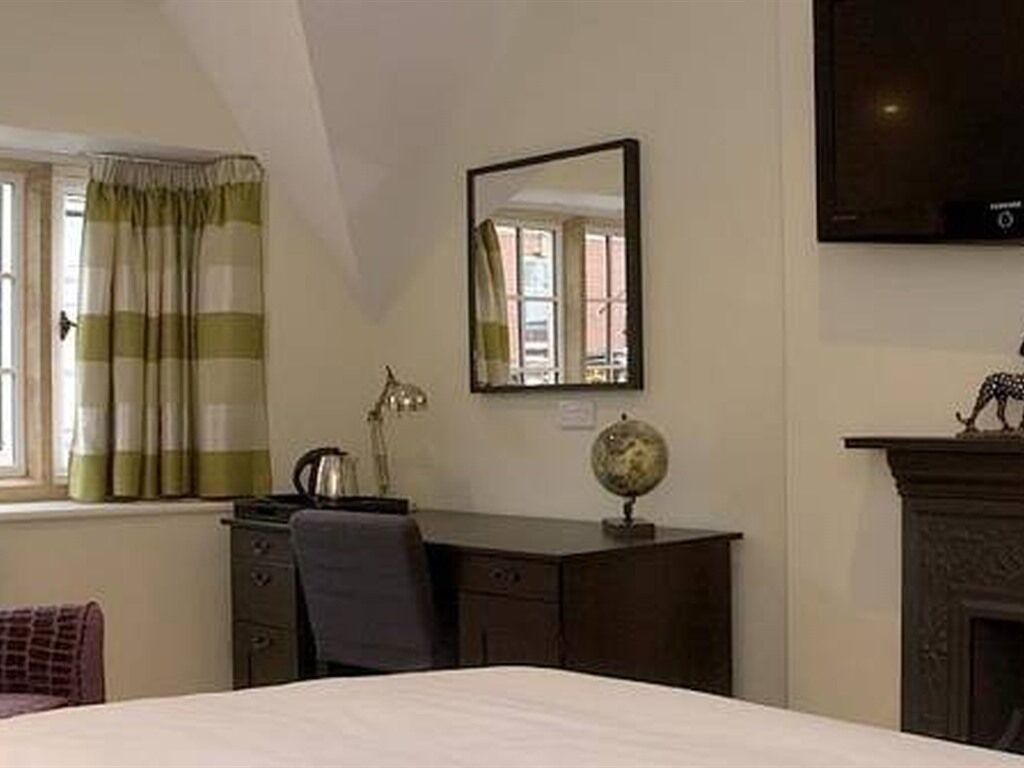 A bedroom with a bed, a desk, a chair, a globe, a mirror, a fireplace, and a window with curtains.