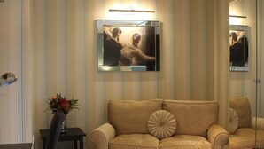 A living room with a beige sofa, a small side table with a vase of flowers, and a television mounted on the wall.