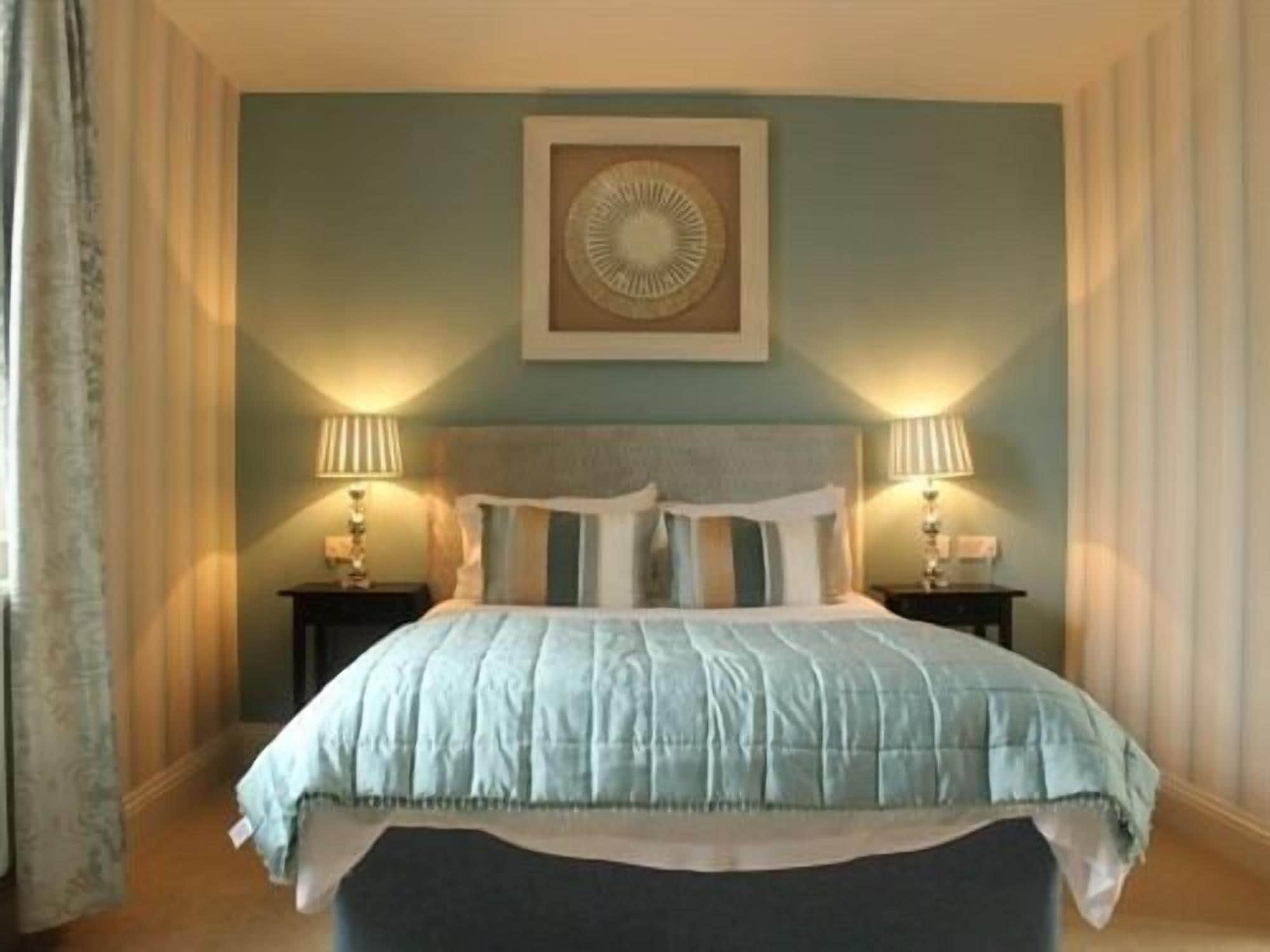 A bedroom with a bed, two bedside tables, and a wall-mounted lamp.
