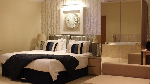 A hotel room with a bed, bedside table, lamp, and a large mirror.