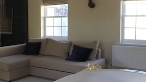 A modern living room with a beige sectional sofa, a large white bathtub, and a window with blinds.