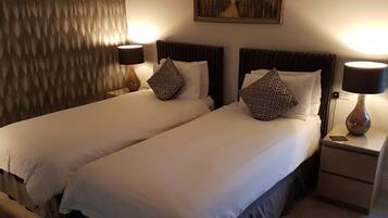 Een hotelkamer met twee bedden, elk voorzien van een kussen, een lamp en een schilderij aan de muur.