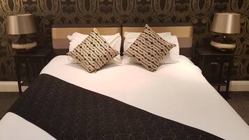 Una cama bien hecha con colcha blanco y negro, dos almohadas estampadas y dos lámparas de noche sobre mesitas a juego.