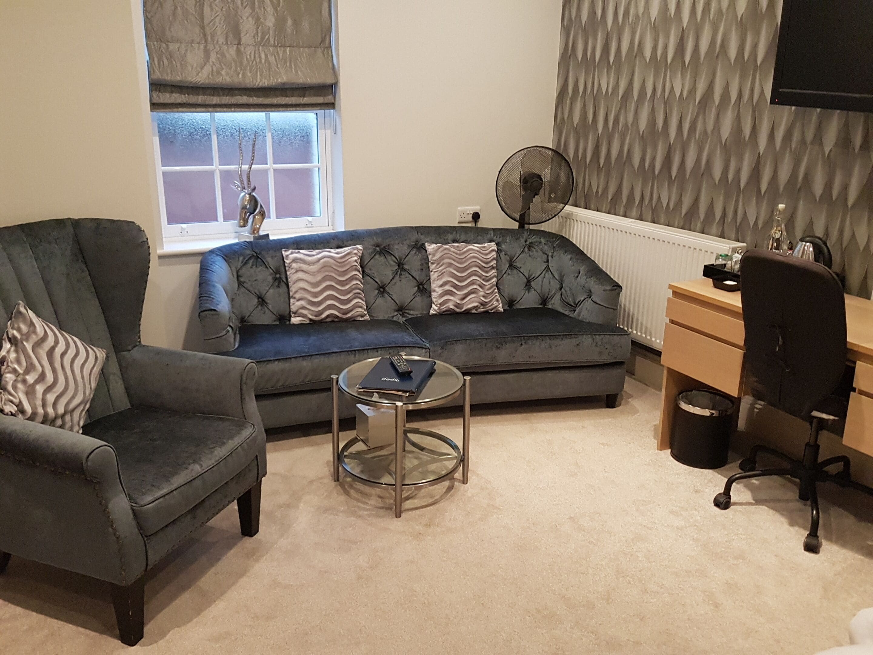 A living room with a grey sofa, two armchairs, a small coffee table, a desk, and a radiator.