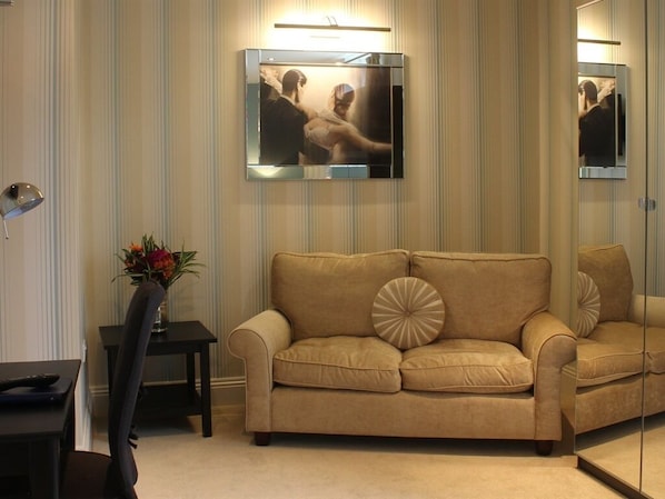 Una habitación con un sofá color beige, una mesita con un florero y un televisor montado en la pared.