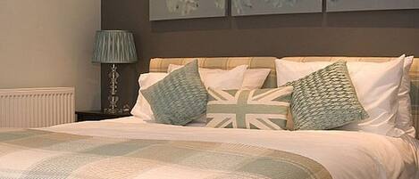 A neatly made bed with a checkered blanket and pillows, a bedside lamp, and a wall with floral artwork.
