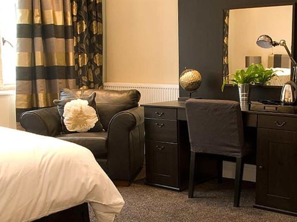 Ein Hotelzimmer mit Bett, Schreibtisch, Stuhl, Kommode, Lampe und Pflanze.
