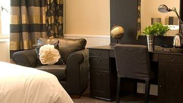 Ein Hotelzimmer mit Bett, Schreibtisch, Stuhl, Kommode, Lampe und Pflanze.