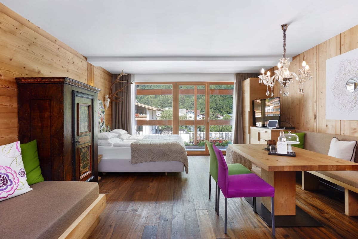 Une chambre à coucher avec un lit, une armoire en bois, une table à manger avec des chaises et une vue sur l’extérieur.