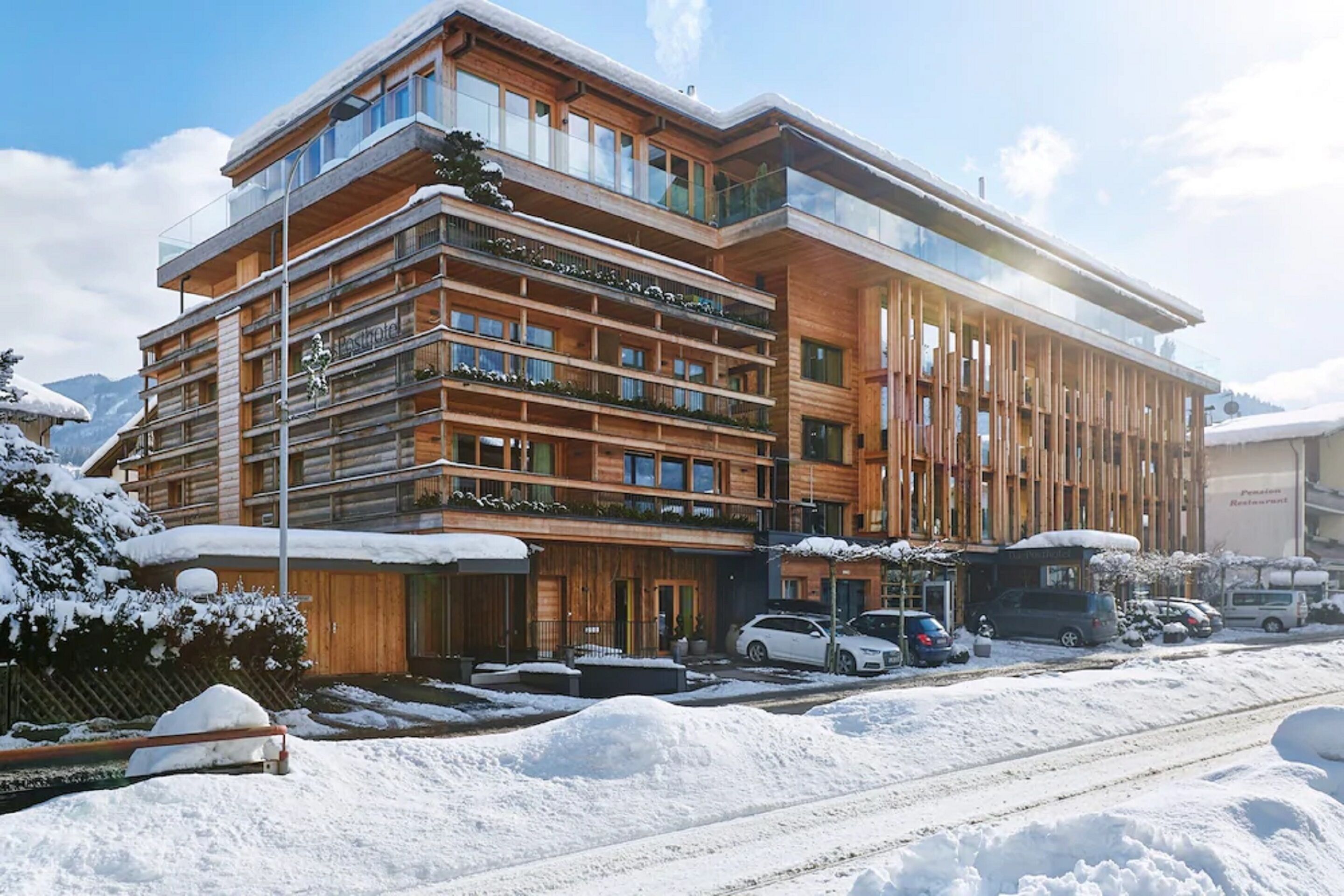 Ett hotell med flera våningar, klätt i trä på utsidan och med balkonger, omgivet av snö och berg.