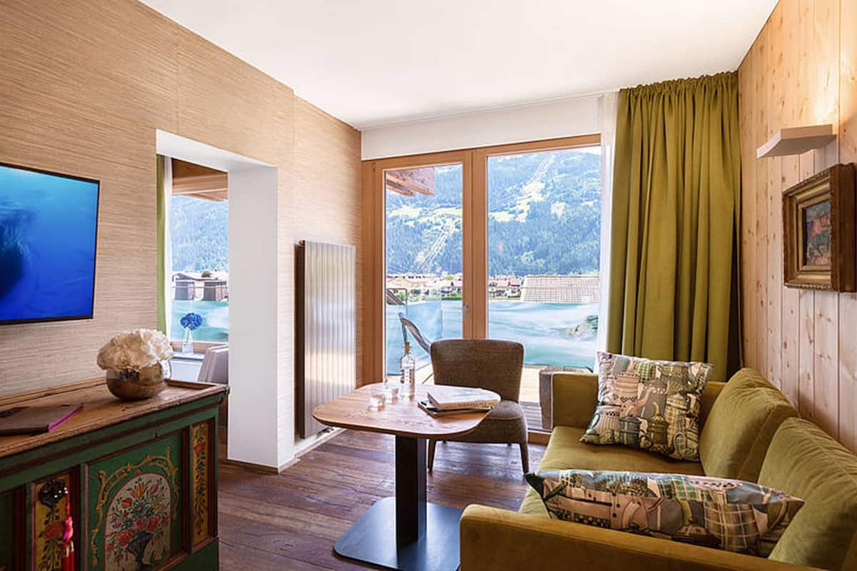 Une pièce dotée d’un plancher en bois, d’un mur en bois, d’une télévision, d’une table avec des chaises, d’un canapé et offrant une vue sur un paysage montagneux grâce à de grandes fenêtres.