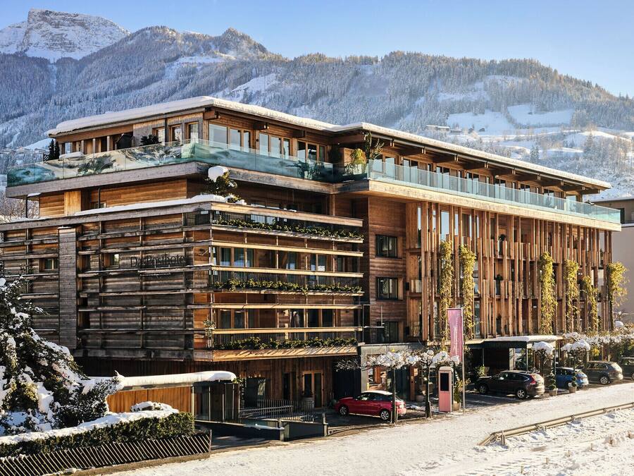 Un hotel moderno con fachada de madera, varios balcones y vistas a montañas nevadas.