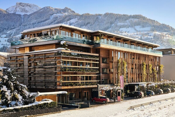 Un hotel moderno con fachada de madera, varios balcones y vistas a montañas nevadas.