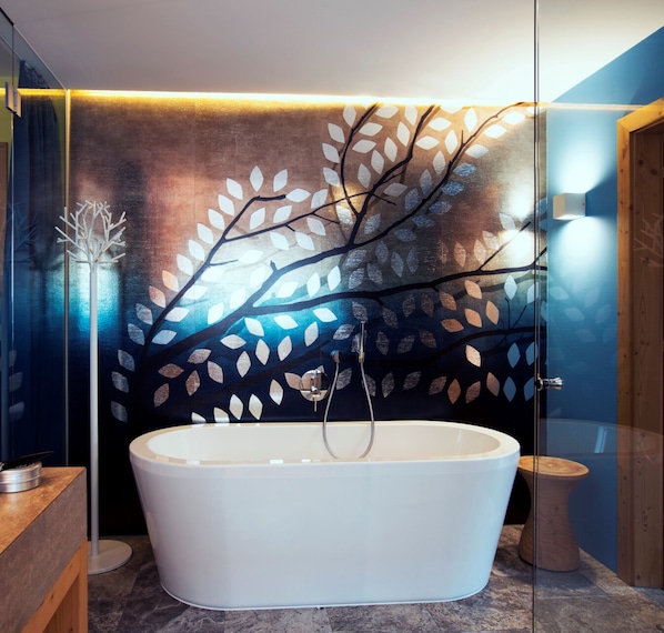 A modern bathroom with a freestanding bathtub, a glass shower enclosure, and a decorative leaf-patterned wall. - DasPosthotel – Boutique Hotel (Zell am Ziller)