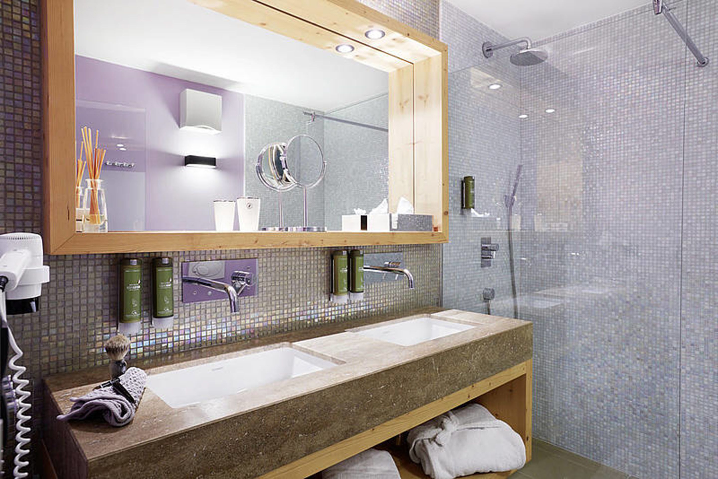 A modern bathroom with a large mirror, two sinks, and a shower area.