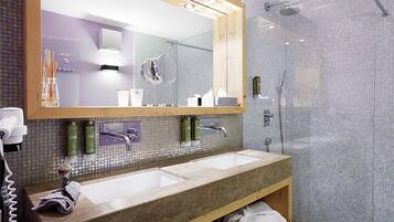 A modern bathroom with a large mirror, two sinks, and a shower area.