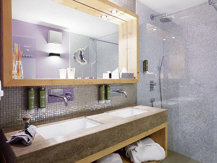 A modern bathroom with a large mirror, two sinks, and a shower area.