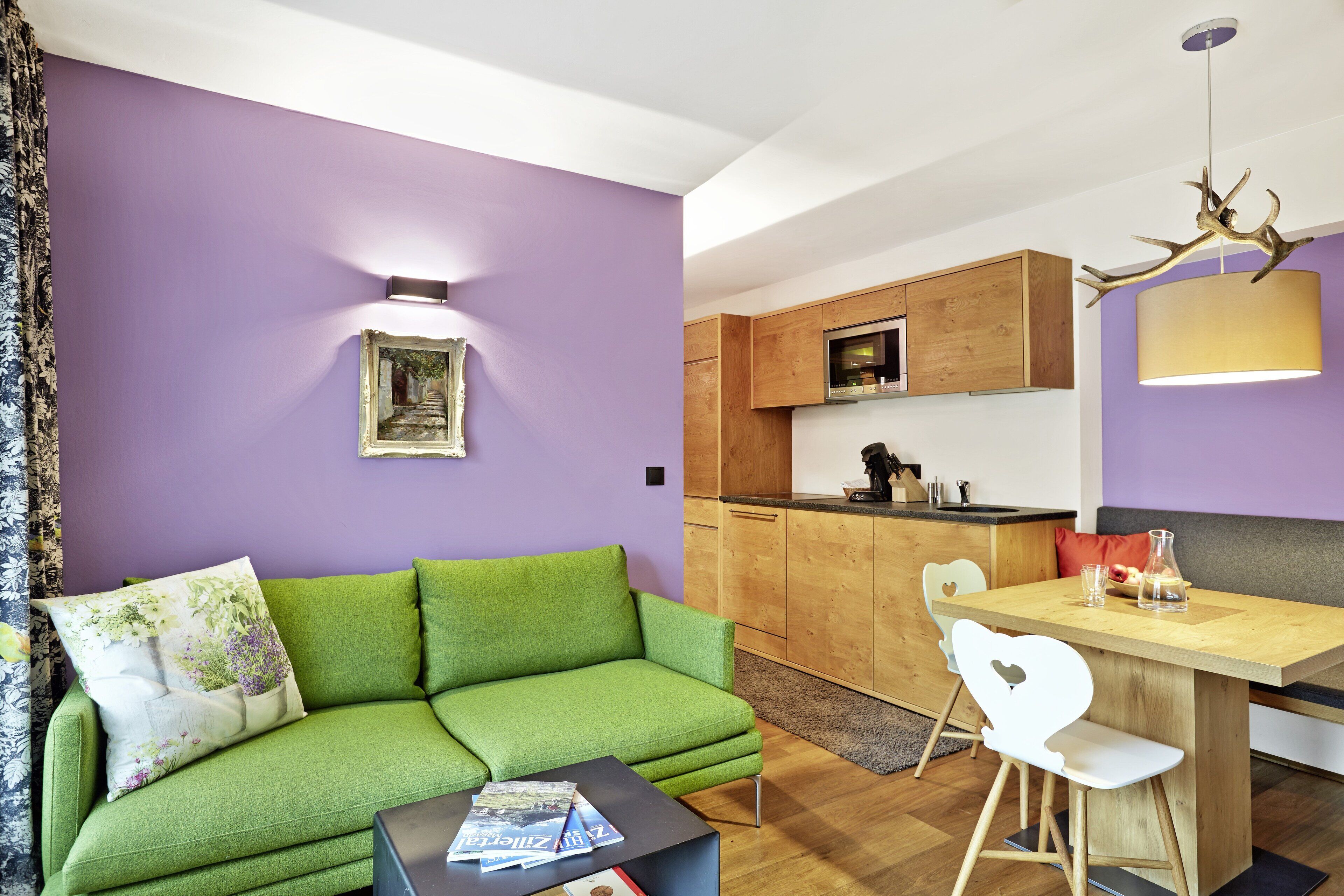 Una sala moderna con un sofá verde, una mesa de comedor de madera y una cocina al fondo.