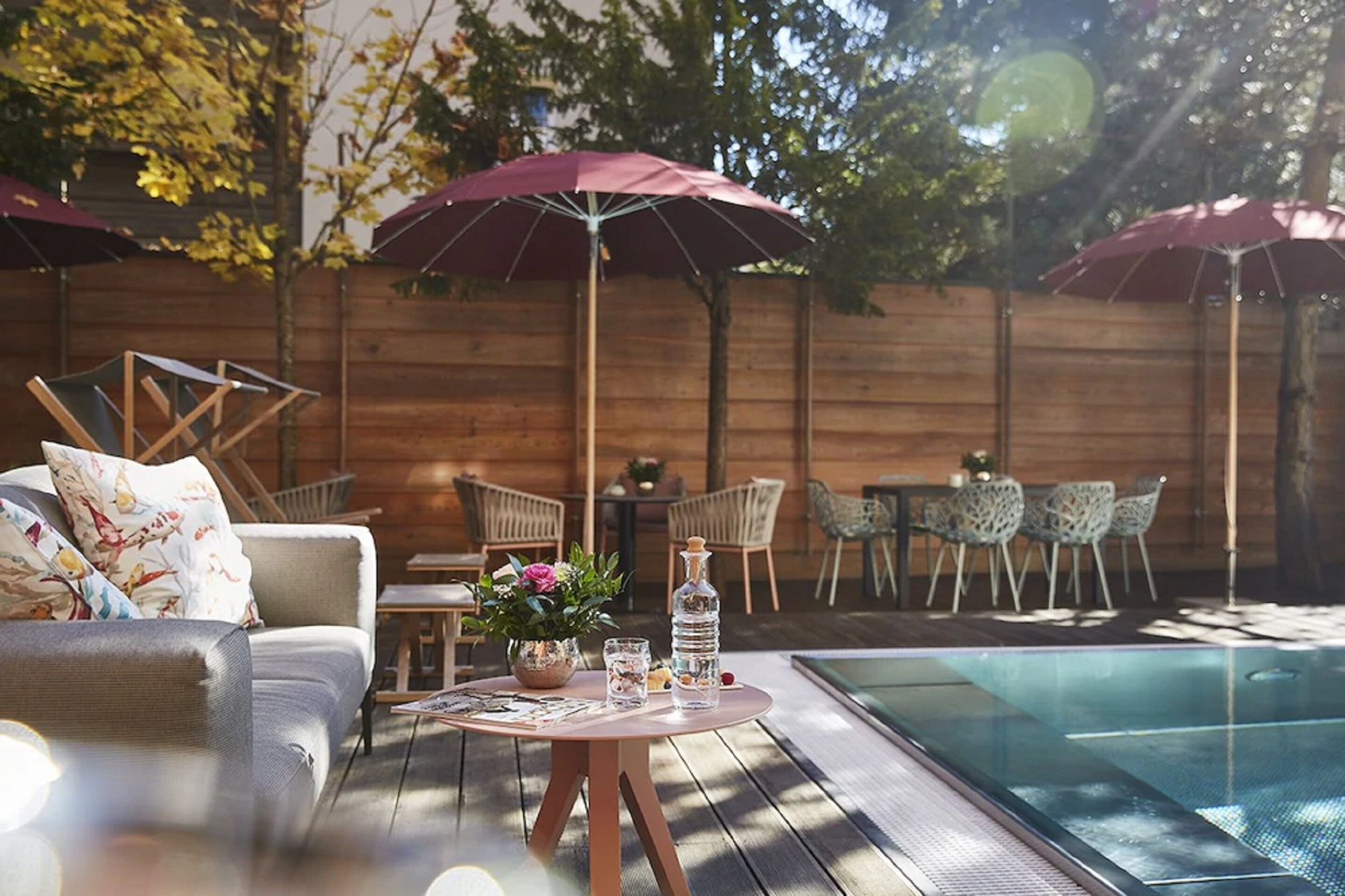 A poolside area with a sofa, chairs, a table with drinks, and umbrellas.