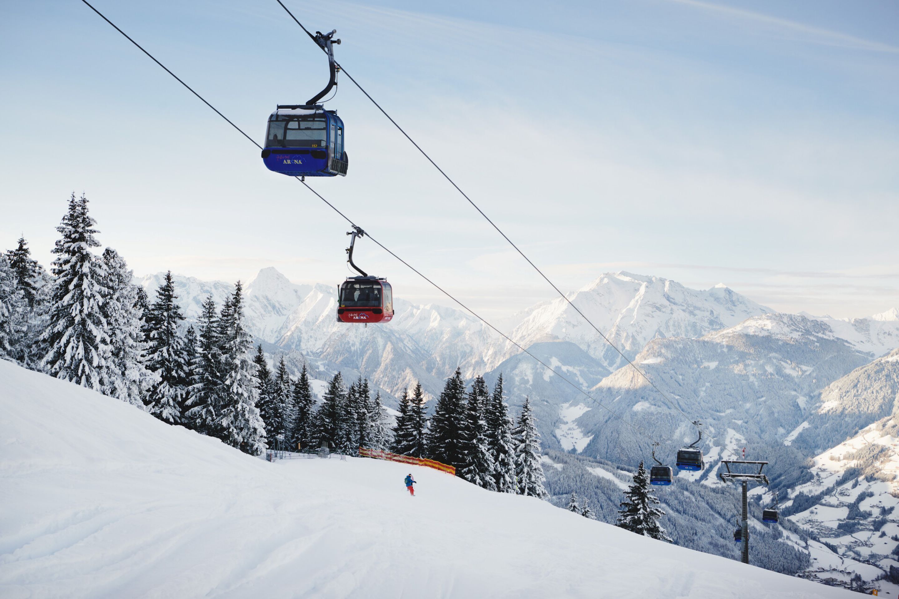 A ski lift with cabins moving up a snowy mountain slope.