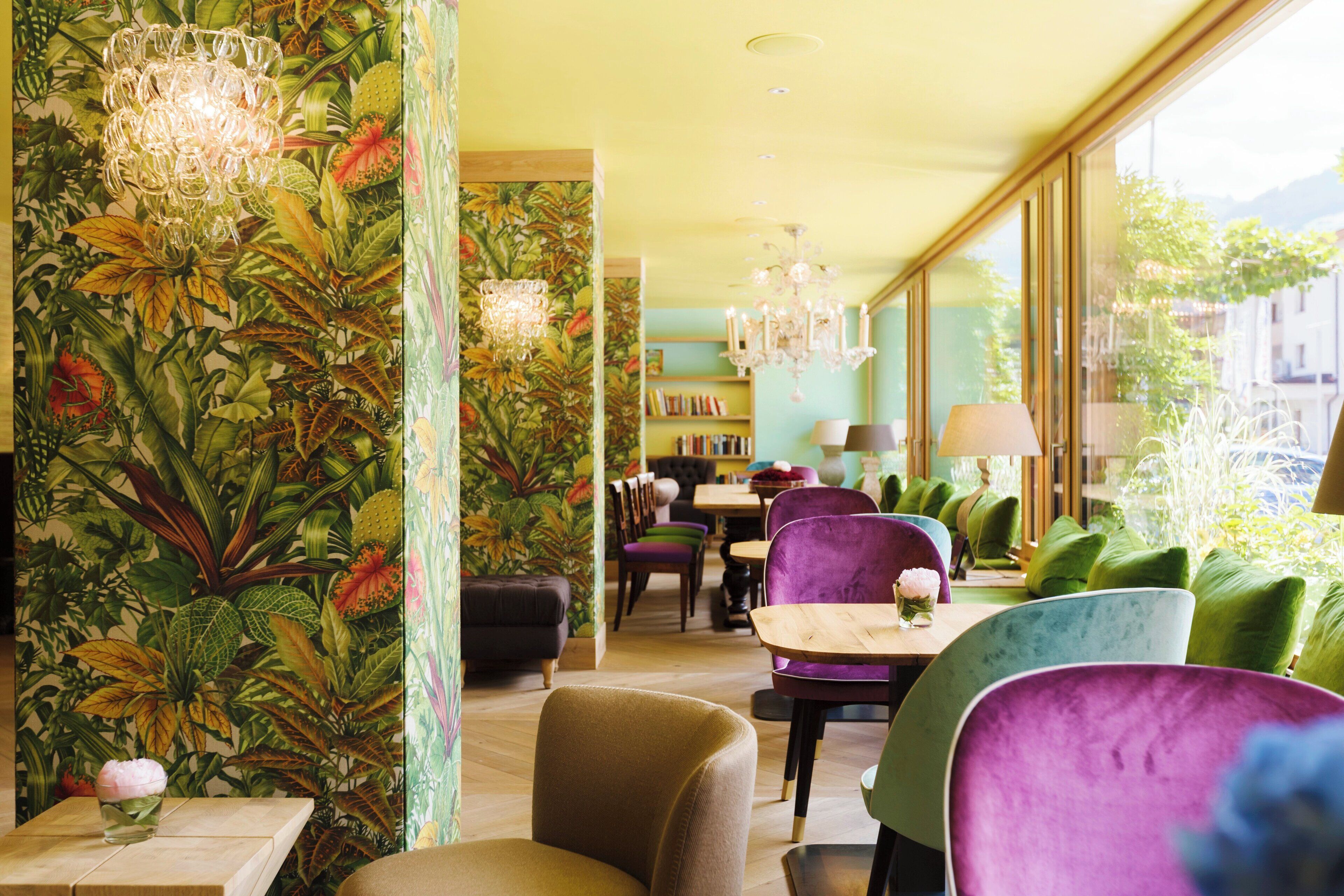 Un restaurante con papel tapiz tropical, sillas coloridas y un candelabro.