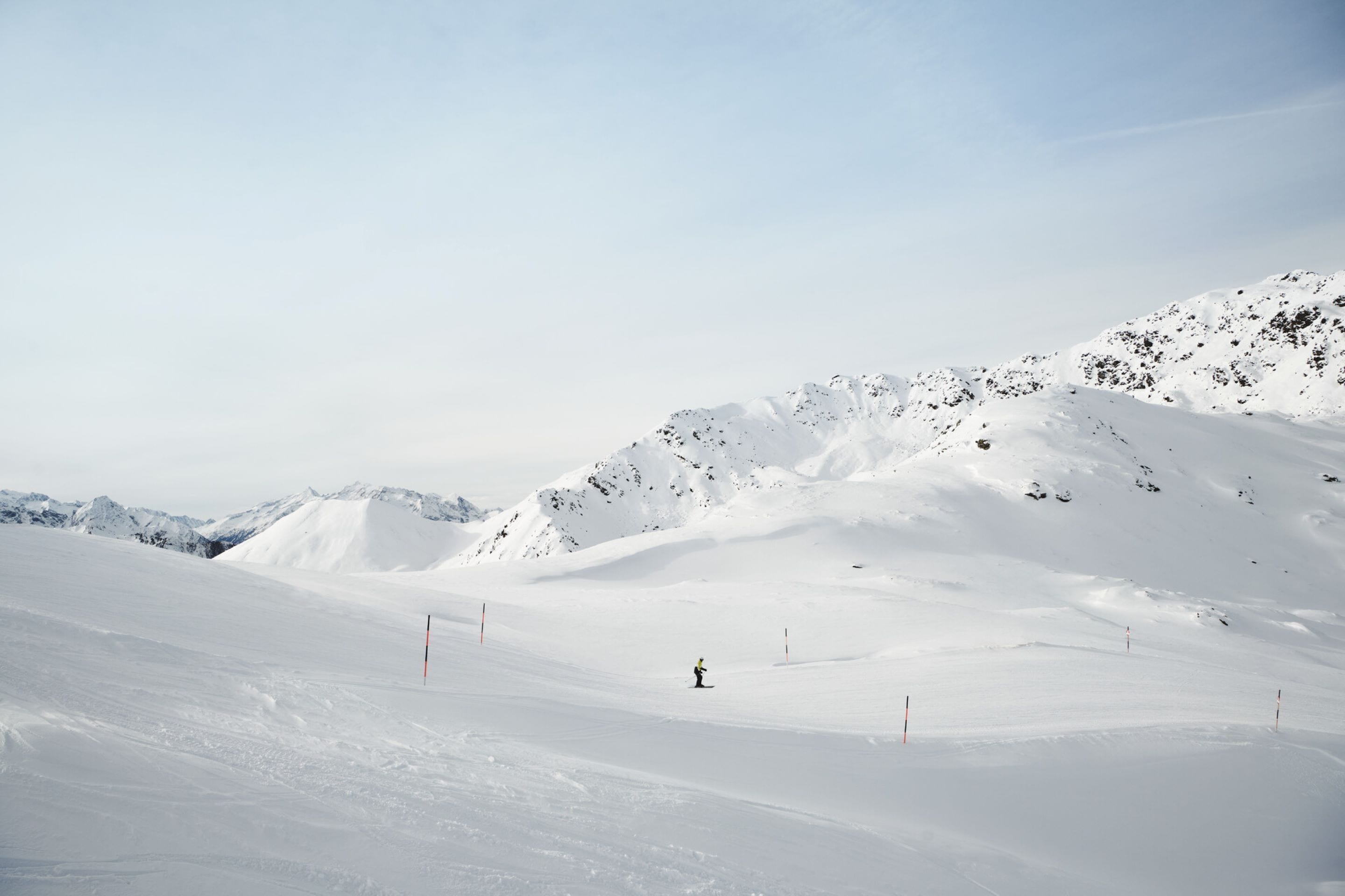 A snow-covered mountain landscape with a skier in the distance.
