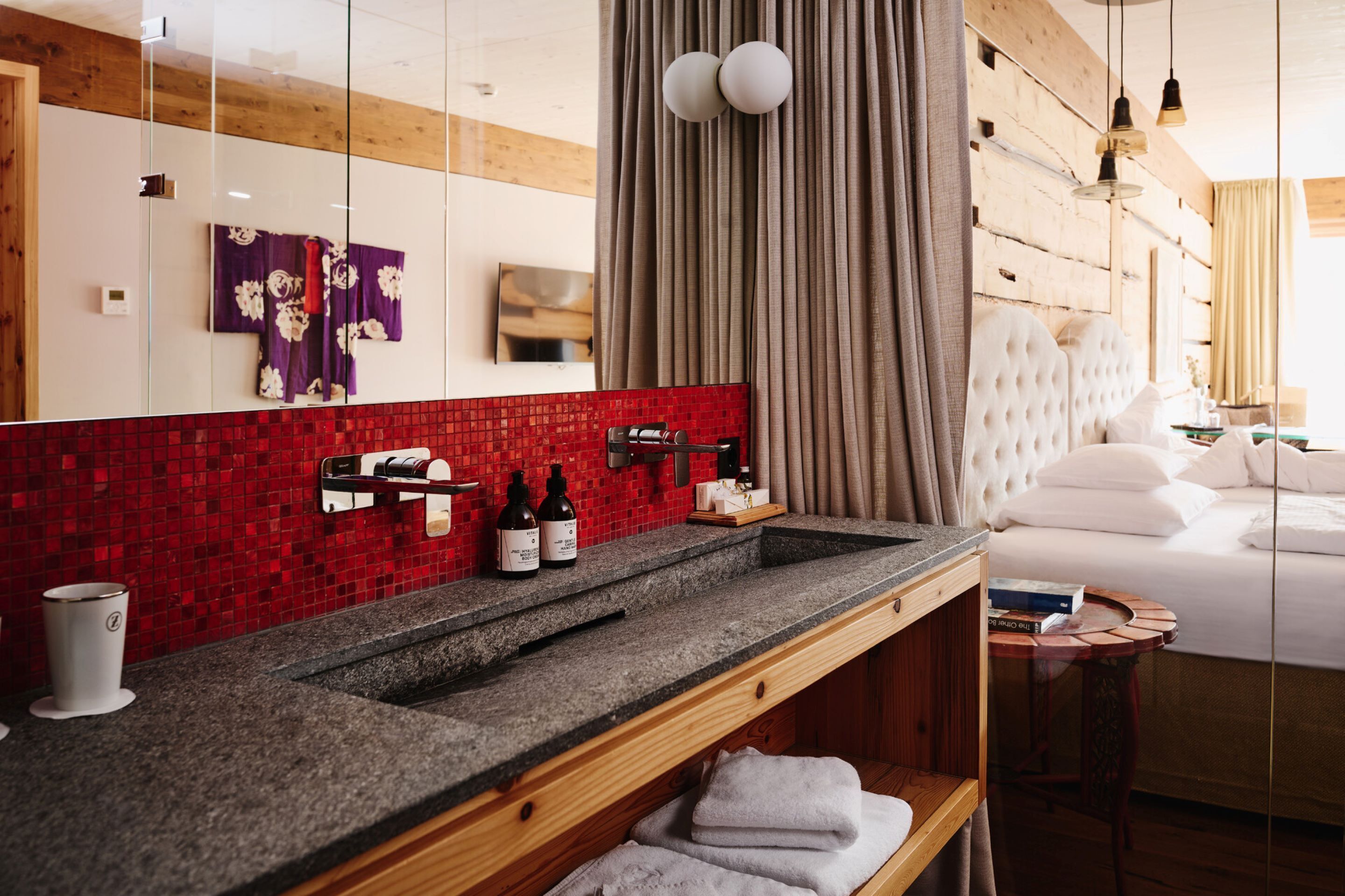Ein modernes Hotelbad mit einer Granit-Arbeitsplatte, einer roten Mosaik-Fassade und einem großen Spiegel.