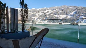 A wooden deck with a view of a green lake and snow-covered mountains. - DasPosthotel – Boutique Hotel (Zell am Ziller)
