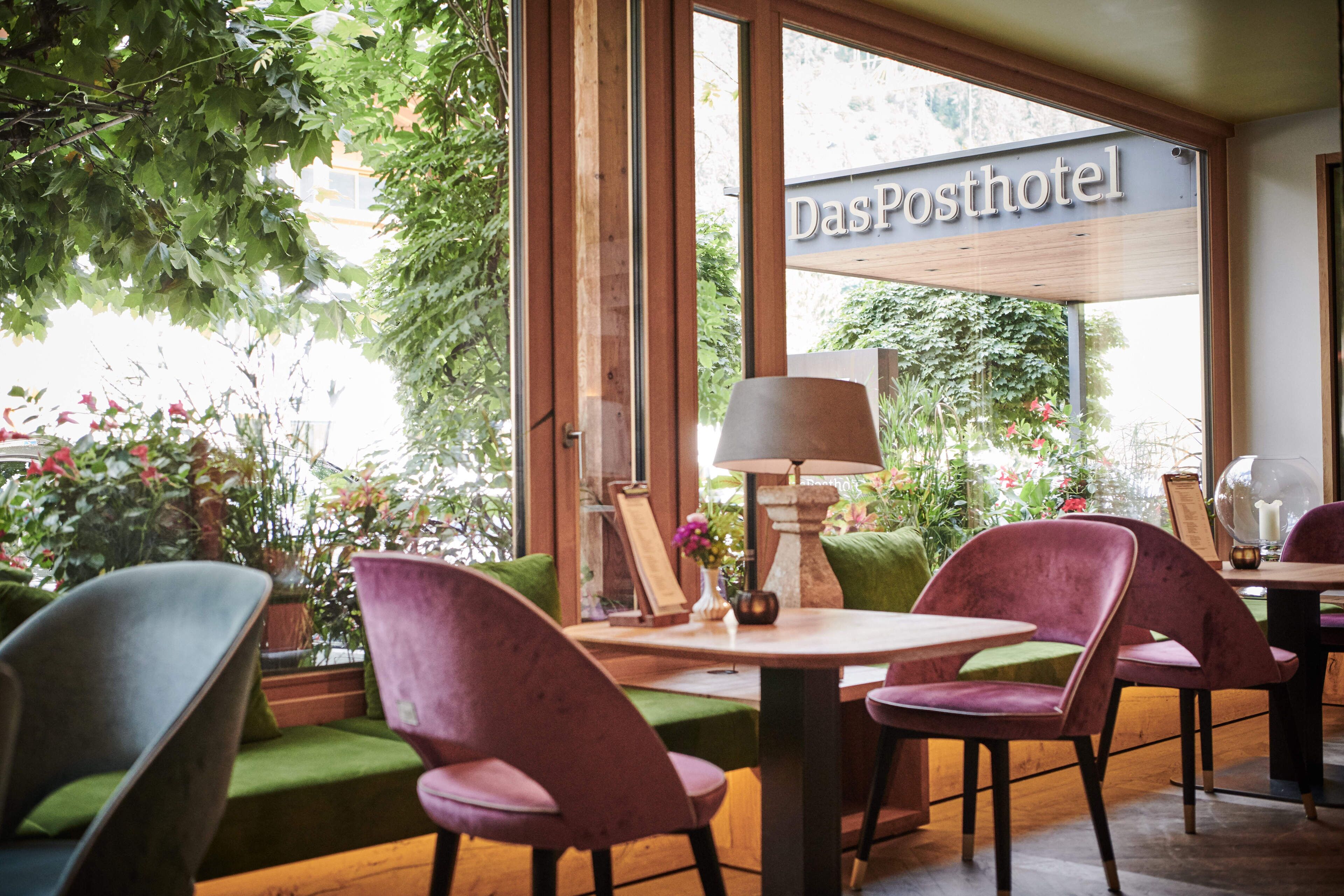 A cozy hotel interior with green upholstered seating, a wooden table, and a sign reading "Das Posthotel".