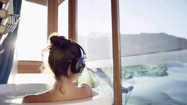 A person in a bathtub with a view of a mountainous landscape through large windows. - DasPosthotel – Boutique Hotel (Zell am Ziller)