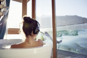 Una persona en una bañera con vistas a un paisaje montañoso a través de amplias ventanas.