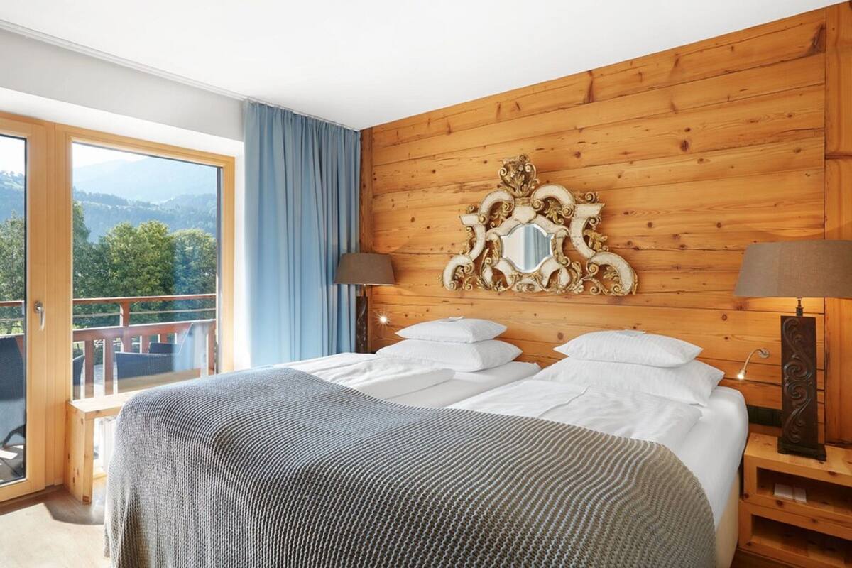 Une chambre dotée d’un grand lit, de murs recouverts de panneaux en bois, d’un balcon offrant une vue dégagée et de deux lampes de chevet.