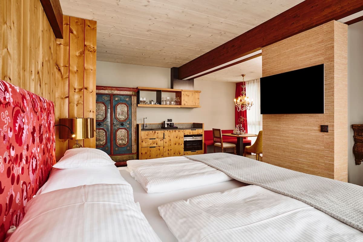 Une chambre d’hôtel avec un grand lit, une armoire en bois, un coin cuisine et un téléviseur fixé au mur.