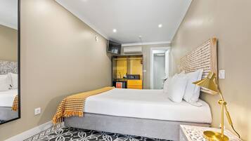 A hotel room with a bed, a bedside table with a lamp, a mirror, a wardrobe, and a bathroom visible through an open door.