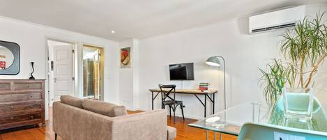 A modern living room with a sofa, a dining table with chairs, a TV, and an air conditioning unit.