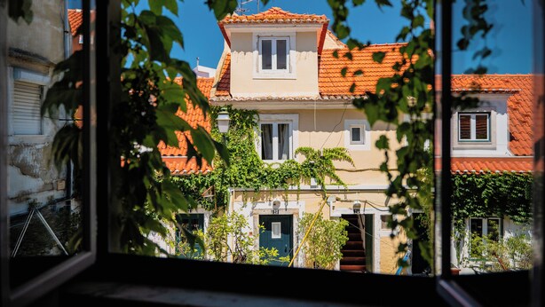 A building with a red-tiled roof, a small balcony, and a door with a number plate. - Casa do Patio by Shiadu (Lisbon)