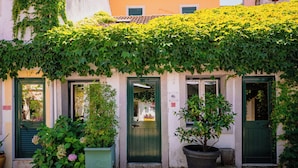 A building with green doors and a covered entrance, surrounded by potted plants and greenery. - Casa do Patio by Shiadu (Lisbon)
