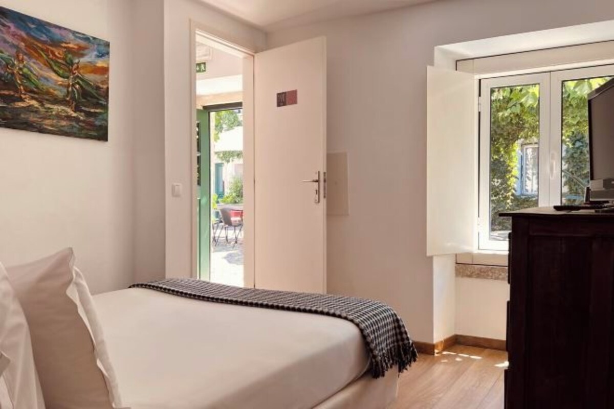 Una camera da letto con un letto, un quadro appeso al muro, una porta che dà su uno spazio esterno e una finestra con vista sul verde.