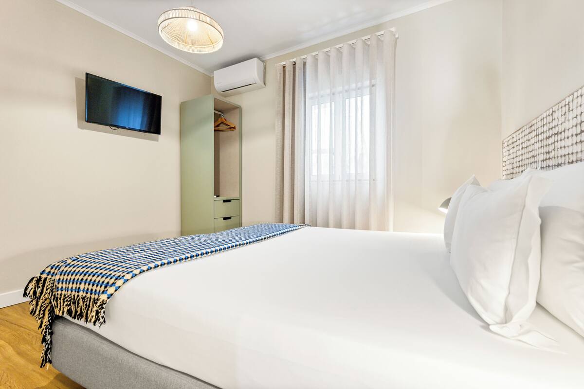 Une chambre d’hôtel avec un grand lit, une télévision, un appareil de climatisation, une armoire et une fenêtre avec des rideaux.